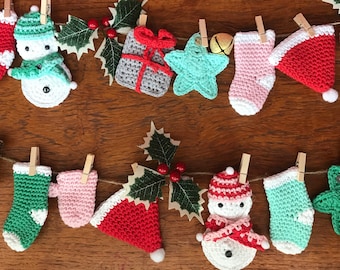 Puede incluir: Una cadena de adornos navideños de crochet colgados en una superficie de madera. Los adornos incluyen un muñeco de nieve, una estrella, una media, una caja de regalo y un gorro de Papá Noel.