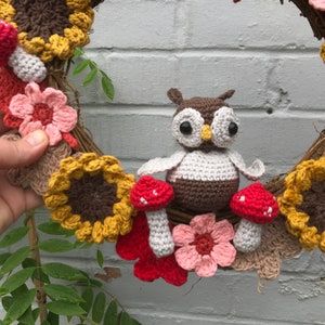 K&ouml;nnte beinhalten: Ein geh&auml;kelter Kranz mit einer braunen und wei&szlig;en Eule, roten und wei&szlig;en Pilzen, gelben Sonnenblumen und rosa Blumen.