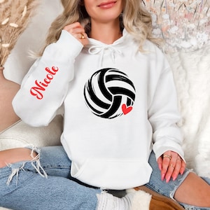 May include: White hoodie with a black and white volleyball graphic and a small red heart. The left sleeve has the name "Nicole" in red script. The hoodie has a drawstring hood and a front pocket.