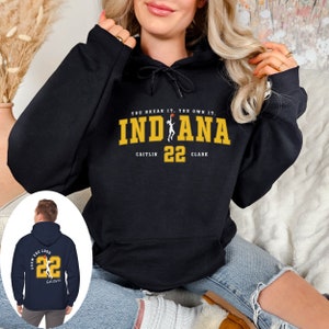 May include: Black hooded sweatshirt with a yellow graphic that says "YOU BREAK IT. YOU OWN IT. INDIANA" with a basketball player silhouette and the text "CAITLIN 22 CLARK". The back of the sweatshirt has a yellow graphic with the text "TEAM 22" and a basketball player silhouette.