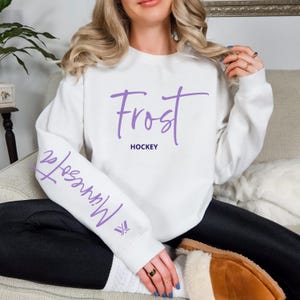 May include: White sweatshirt with purple text that says "Frost Hockey" on the front and "Minnesota Frost" on the left sleeve.