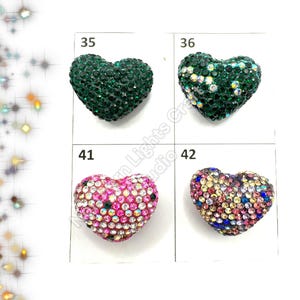 May include: Four heart-shaped embellishments with different colored rhinestones. The embellishments are labeled 35, 36, 41, and 42. The embellishments are green, green, pink, and multi-colored.