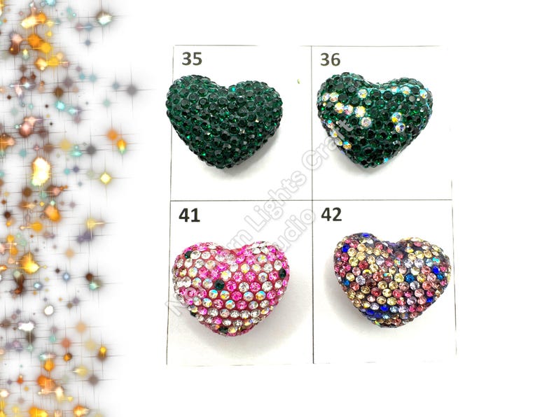 May include: Four heart-shaped embellishments with different colored rhinestones. The embellishments are labeled 35, 36, 41, and 42. The embellishments are green, green, pink, and multi-colored.