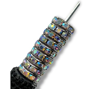 May include: A close-up of a decorative pen featuring a series of iridescent, crystal-like rings. The rings are set in silver-toned metal and are stacked along the pen's shaft. The pen's base is black and textured, and the tip is silver.