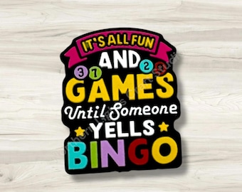 May include: A black sticker with colourful text that reads: IT'S ALL FUN AND GAMES UNTIL SOMEONE YELLS BINGO. The design features yellow, white, purple, red, and teal lettering, along with small numbered circles and yellow stars.
