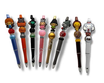 May include: Eight pens featuring character toppers and decorative beads. The pens have colorful barrels in blue, orange, black, pink, gold, gray, dark red, and white. Each topper depicts a different figure, including a girl, dog, witch, fairy, boy, robot, lion, and monkey.