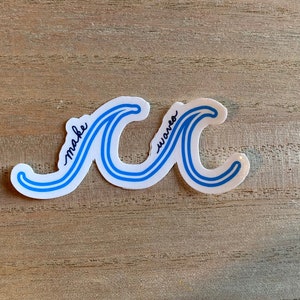 May include: A white sticker with two blue waves, one above the other. The words "make waves" are written in black cursive on the waves.