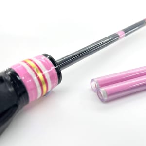 May include: A black tool with a pink and gold striped handle and a black shaft. Two pink tubes are next to the tool. The tool has a pink and gold striped band near the top.