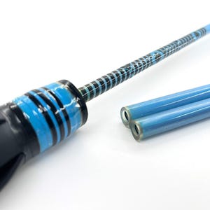 May include: A close-up of a tool with a black handle and blue and black striped accents. The shaft is blue with a patterned design. Two additional blue tubes are also visible, suggesting a set or related components.