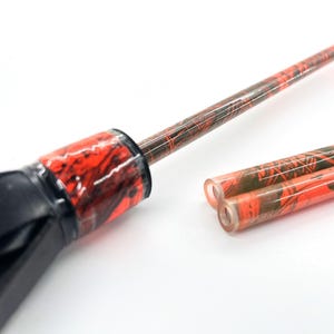 May include: Close-up of a black and red tool with a long, thin shaft and two additional tubes. The shaft and tubes have a red and black marbled pattern. The tool's handle is black.