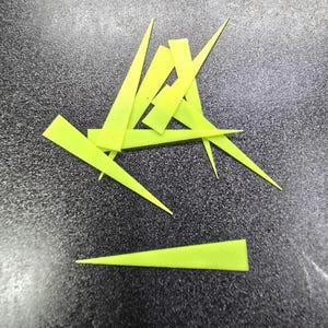 May include: A pile of bright yellow plastic craft sticks, also known as skewers, arranged on a dark gray surface.