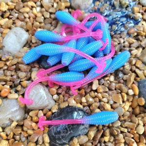 May include: A pile of blue and pink soft plastic fishing lures. The lures are shaped like worms and have a ribbed texture.