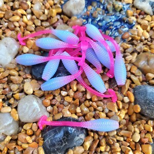 May include: A group of purple and pink fishing lures with a worm shape. The lures are made of soft plastic and have a ribbed texture.