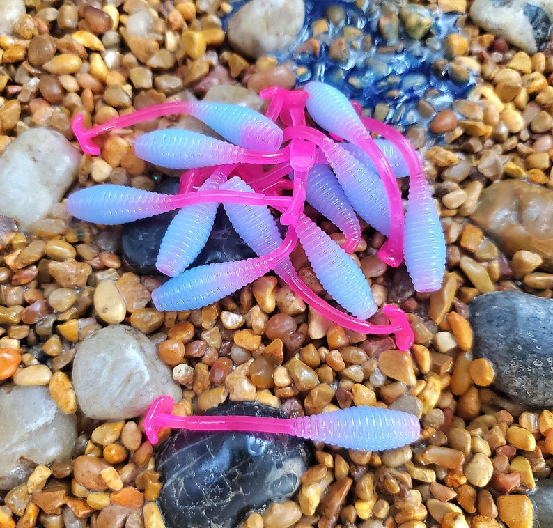 May include: A group of purple and pink fishing lures with a worm shape. The lures are made of soft plastic and have a ribbed texture.