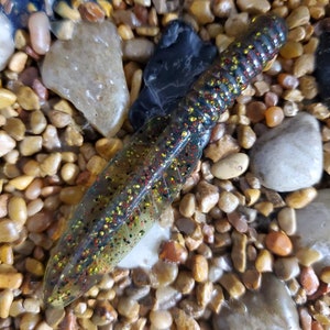 May include: A translucent, segmented, worm-shaped fishing lure with a speckled, multi-colored pattern of black, red, yellow, and gold.