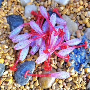 May include: A pile of pink and red fishing lures with glitter. The lures are shaped like worms and have a red tail.