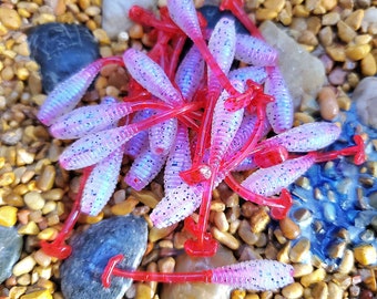 May include: A pile of pink and red fishing lures with glitter. The lures are shaped like worms and have a red tail.