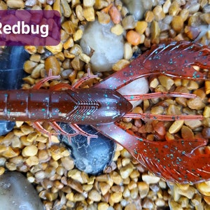 May include: Redbug crawfish lure with a red and green speckled finish. The lure is designed to resemble a crawfish and has realistic claws and antennae.