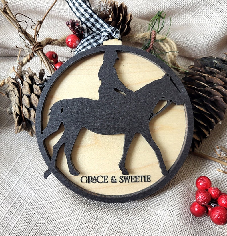 May include: A round wooden ornament with a black silhouette of a person riding a horse. The ornament is decorated with the text "GRACE & SWEETIE".