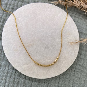 Könnte beinhalten: Eine goldene Kettenkette mit einer Reihe kleiner goldener Perlen in der Mitte.