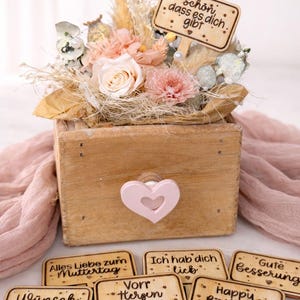 May include: A white ceramic mug with a black handle and the text "But First, Coffee" in a bold, black font. The mug is set against a blurred background, suggesting a cozy setting.