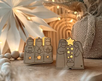 May include: Wooden nativity scene figurines with cutout designs. The figurines depict the three wise men and the holy family, with star and lantern cutouts. The figures are illuminated with warm light, creating a festive holiday decoration.