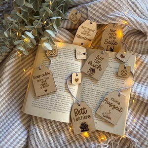 Peut inclure: Une collection de marque-pages en bois clair avec du texte et des icônes gravés, incluant des phrases comme Keep calm Drink Tea and read a Book, Zeit für mich, Bett Lektüre, Kleine Auszeit, Auf dieser Seite warten Abenteuer et Nur noch eine Seite.