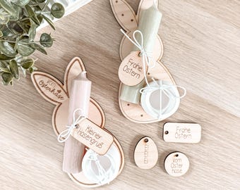 May include: Wooden Easter bunny decorations with candles and tags. The bunnies are light brown with small polka dots. The candles are pink and green. The tags say "Frohe Ostern" and "Kleiner Hasengruß".
