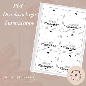 Puede incluir: Una hoja de pegatinas blancas con un patrón de corazones y puntos negros. Cada pegatina tiene las palabras "NUR EINE Kleinigkeit" en negro. También se ven las palabras "PDF Druckvorlage Tütenklappe".