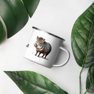 Puede incluir: Taza de camping de esmalte blanco con una ilustración en blanco y negro de un pequeño animal parecido a un cerdo rayado. El animal tiene un hocico marrón y está de pie sobre un fondo blanco.