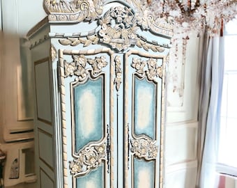 May include: A large, ornate, two-door armoire with a light blue and gold finish. The armoire has intricate carvings and a decorative top.