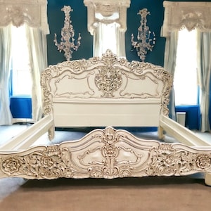 May include: White ornate wooden bed frame with intricate carvings and a high headboard. The bed frame is in a bedroom with blue walls and white curtains.