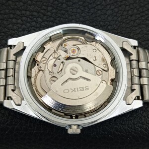May include: A silver-toned Seiko watch with a visible mechanical movement. The watch's back is open, revealing the intricate internal gears, springs, and the word "SEIKO" on a silver plate. The watch band is also silver-toned.