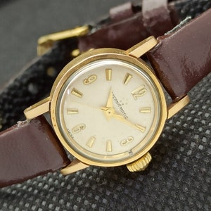 May include: A gold-tone wristwatch with a white face and black hands. The watch has a brown leather band and says "Ternomatic Swiss" on the face.