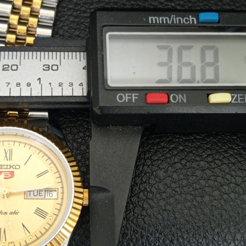 Peut inclure: Gros plan d'une montre Seiko dor&eacute;e mesur&eacute;e avec un pied &agrave; coulisse num&eacute;rique. L'&eacute;cran affiche 36,8 mm. Le cadran indique le mardi 16. L'outil est r&eacute;gl&eacute; en mm/pouce.
