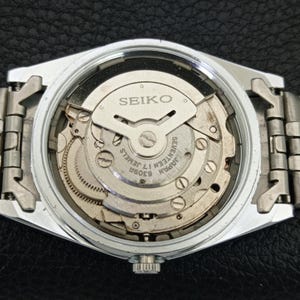 May include: A silver-toned Seiko watch with a clear back, showcasing the intricate internal mechanism. The watch face displays the Seiko logo and text indicating "Seventeen 17 Jewels" and "Japan 6309A". The watch band is also silver-toned.
