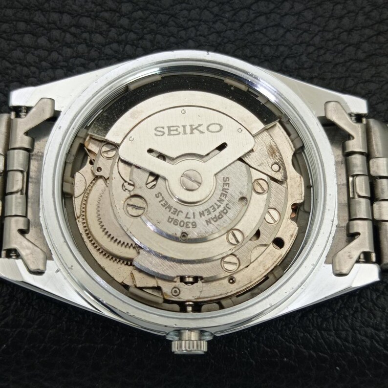 May include: A silver-toned Seiko watch with a clear back, showcasing the intricate internal mechanism. The watch face displays the Seiko logo and text indicating "Seventeen 17 Jewels" and "Japan 6309A". The watch band is also silver-toned.