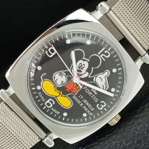 May include: A silver-tone wristwatch with a square case and a mesh metal band. The black dial features a graphic of Mickey Mouse, white Arabic numerals at 3, 6, 9, and 12, and the text Fortis, 17 Jewels, Shock Proof, and Swiss Made.