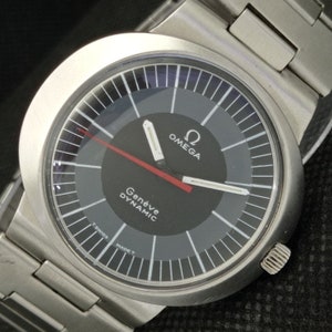 Pode incluir: Um relógio de pulso Omega Genève Dynamic prateado com um mostrador preto e um ponteiro de segundos vermelho. O relógio tem uma pulseira prateada e um mostrador redondo.