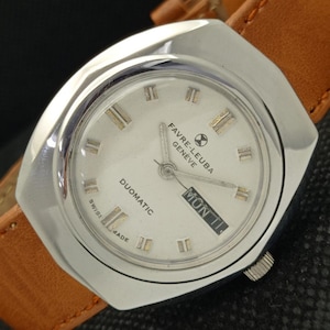 May include: A silver wristwatch with a white face and black hands. The watch has a day and date display and says "Favre-Leuba Genève Duomatic" on the face.