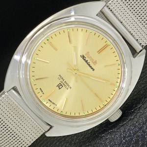 Może przedstawiać: Srebrny zegarek na rękę ze złotą tarczą. Tarcza zegarka ma czarne oznaczenia i tekst "Seiko  Kihinasar  Para Shock 17 Jewels  R2  Made in Japan  M024 0221 A".