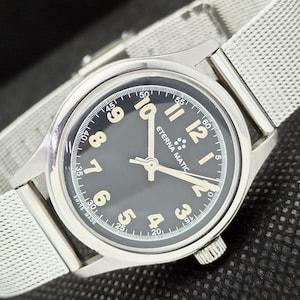 May include: A silver wristwatch with a black face and white markings. The watch has a silver metal band and says "Eterna Matic" on the face.