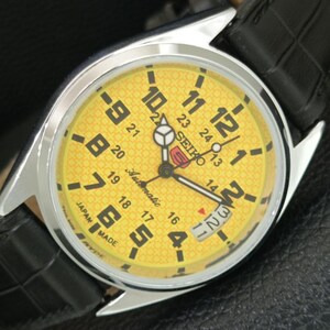 May include: A Seiko 5 automatic wristwatch with a bright yellow dial featuring a geometric pattern, large black Arabic numerals, a 24-hour inner scale, and a date window. The watch has a polished silver-tone metal case and a black leather strap.