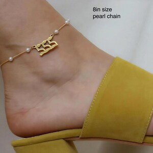 A gold ankle bracelet with a charm on a person's ankle wearing yellow sandals.