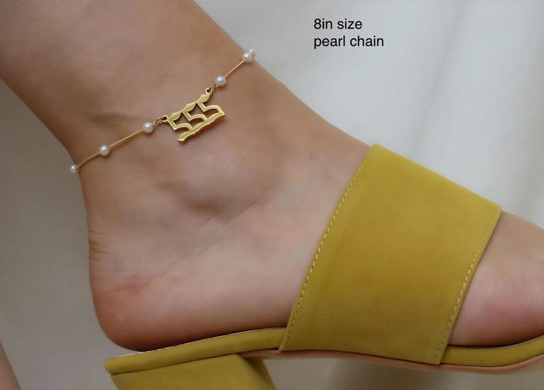 A gold ankle bracelet with a charm on a person's ankle wearing yellow sandals.