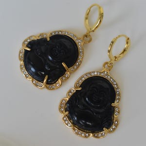 A pair of gold earrings with black Buddha-shaped pendants and rhinestones.