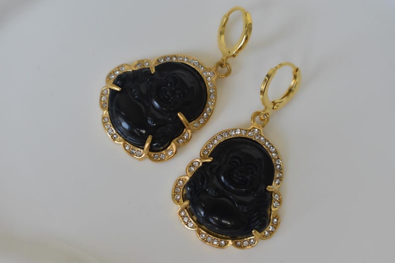 A pair of gold earrings with black Buddha-shaped pendants and rhinestones.
