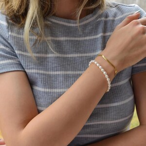 A close-up of a person's arm wearing a gray and white striped shirt, with a bracelet and a necklace visible.