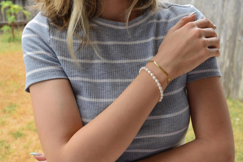 A close-up of a person's arm wearing a gray and white striped shirt, with a bracelet and a necklace visible.