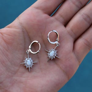 A hand holding a pair of silver earrings with star-shaped charms.